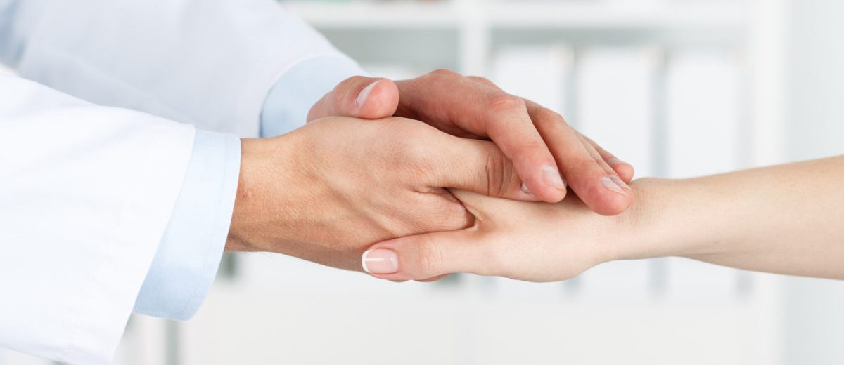 Friendly male doctor's hands holding female patient's hand for encouragement and empathy.