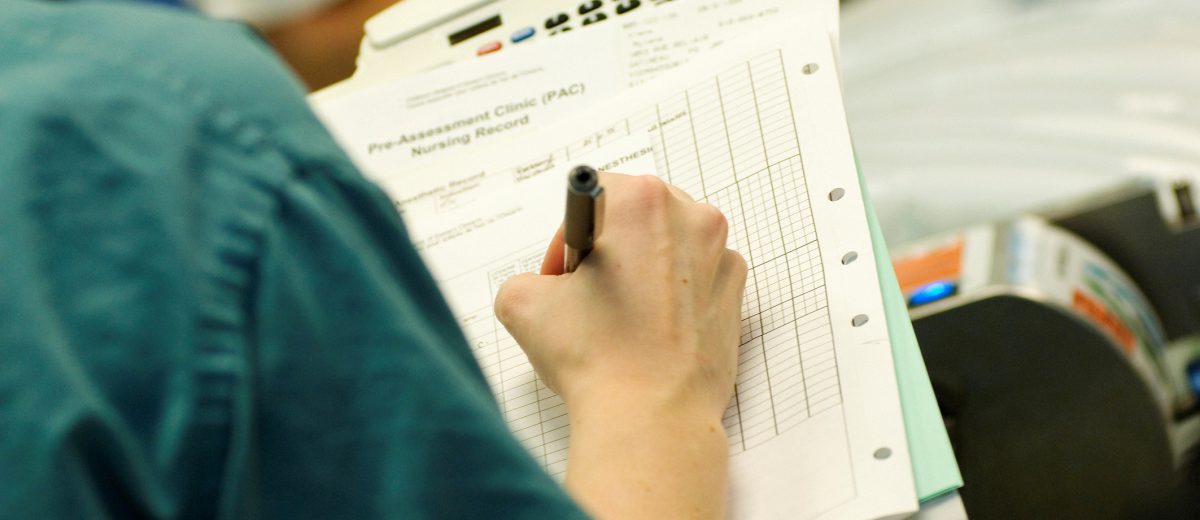 Surgical nurse writing on patient chart.